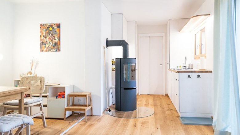 Moderner Wohnbereich mit Holzfußboden, Kaminofen, Esstisch und Küchenzeile.