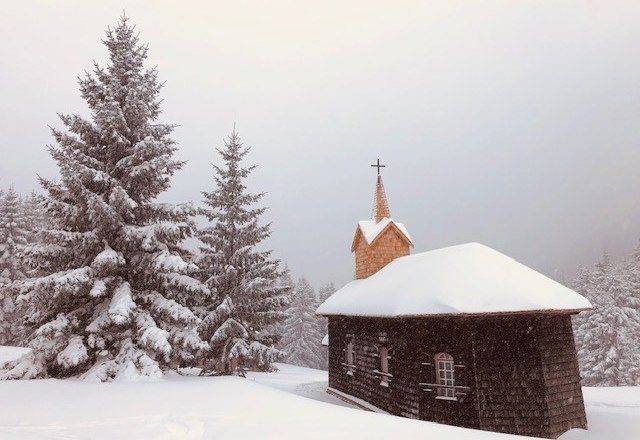 Eine kleine Kirche im Schnee mit Tannenbäumen im Hintergrund.