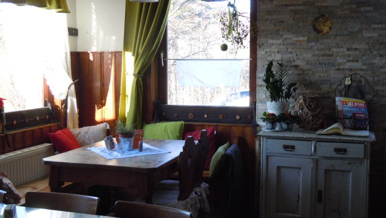 Gemütliche Ecke in einem Raum mit Holztisch, Kissen und Pflanzen.