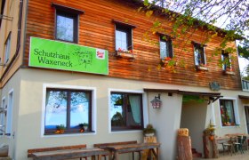 Eingang zum Schutzhaus Waxeneck mit Holztischen und Blumenkästen.
