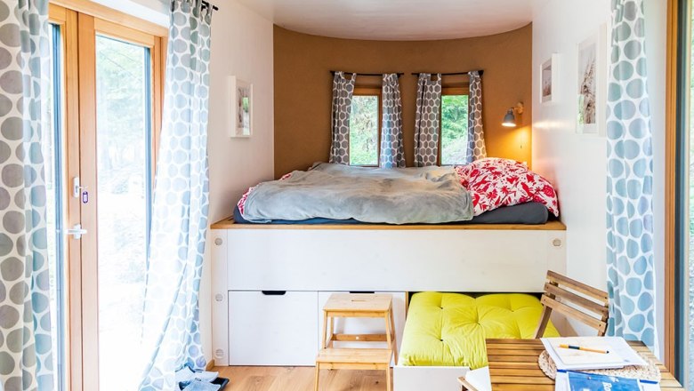 Gemütlicher Schlafbereich mit Hochbett, Vorhängen und kleinem Tisch in einem hellen Raum.