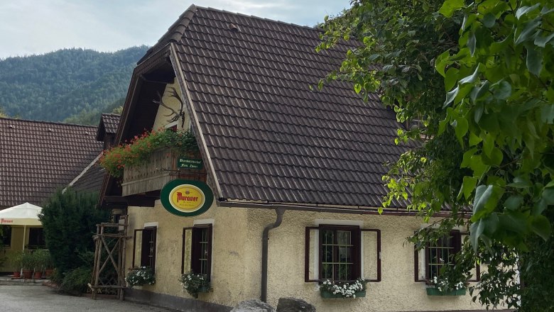 Traditionelles Gasthaus mit Blumen und Murauer-Schild, umgeben von B&auml;umen.