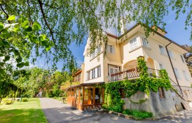 Ein gelbes Herrenhaus mit Efeu bewachsen, umgeben von Bäumen und einem Gartenweg.