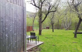 Holzscheune neben Obstgarten mit Tisch und Stühlen auf Holzterrasse.