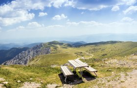 Panoramablick von einem Berg mit einer Bank im Vordergrund und grünen Hügeln im Hintergrund.
