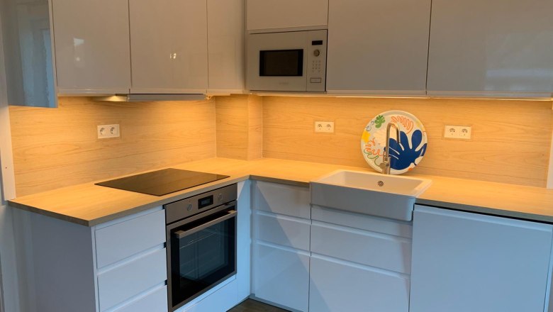 Moderne Küche mit weißen Schränken, Holzarbeitsplatte, eingebautem Ofen und Spüle.