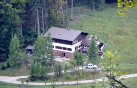 Ein großes Haus im Wald mit einem Auto davor, umgeben von Bäumen und Wiesen.