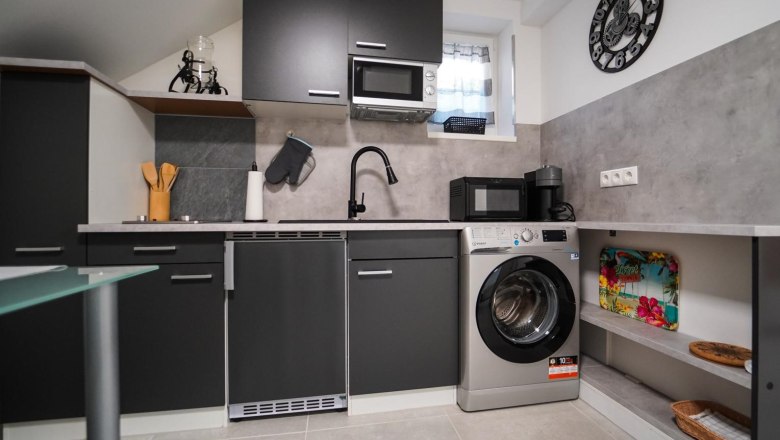 Moderne Küche mit schwarzen Schränken, Waschmaschine, Mikrowelle und Kaffeemaschine.