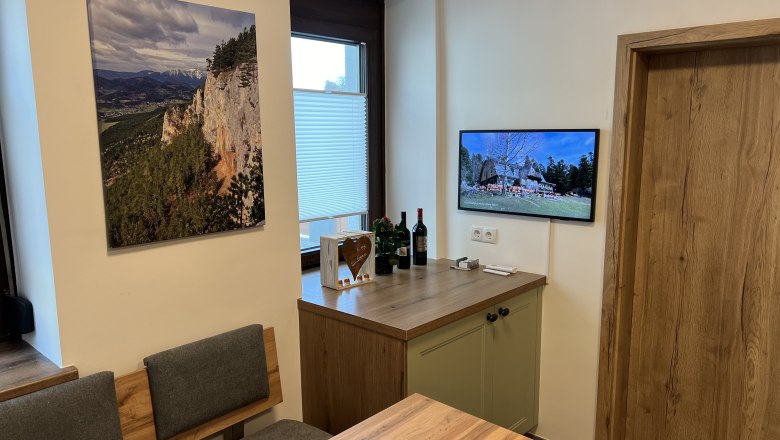 Küche mit Holzmöbeln, einem Landschaftsbild an der Wand und einem Fernseher, der ein Bild von einem Haus zeigt.