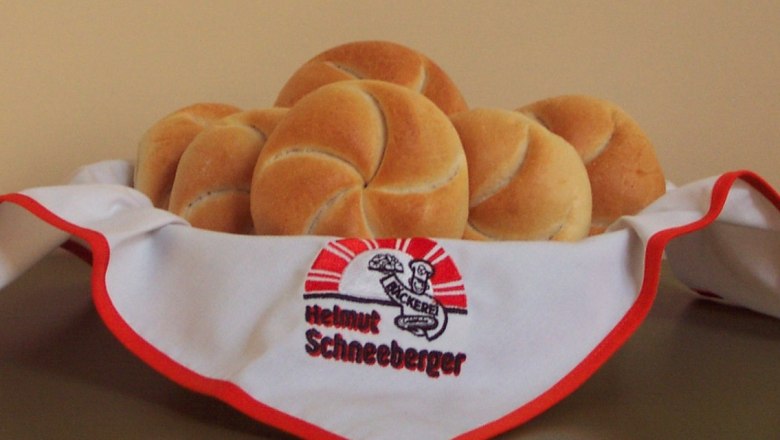 Ein Korb mit frischen Brötchen, bedeckt mit einer Serviette der Bäckerei Helmut Schneeberger.