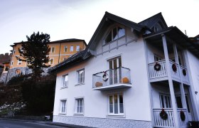 Zwei Häuser, eines weiß mit Balkon, das andere gelb, mit Dekoration.
