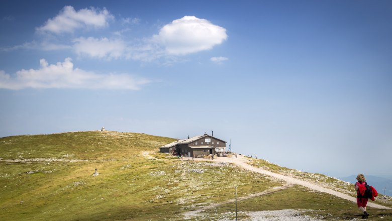 Eine Berghütte auf einem Hügel mit blauem Himmel und Wolken im Hintergrund.