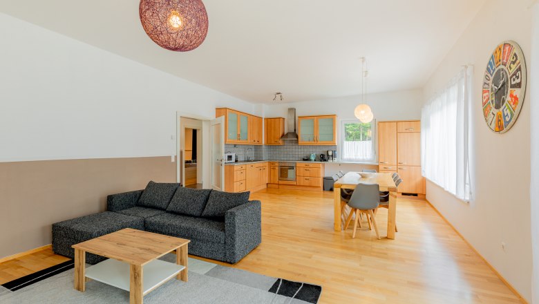 Offener Wohnbereich mit K&uuml;che, Esstisch und Sofa.