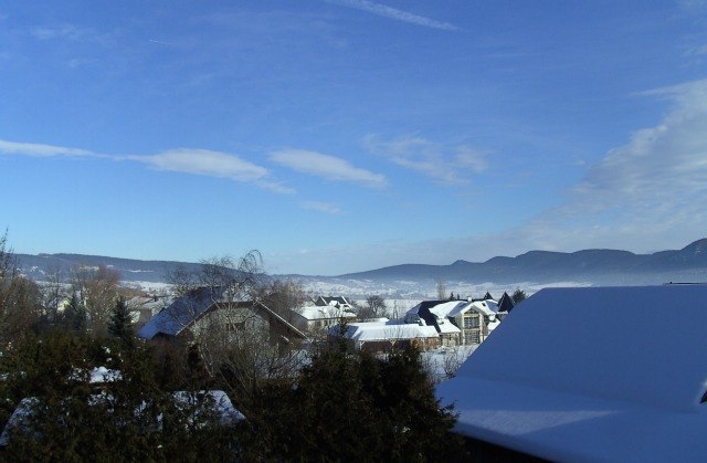 Winterlandschaft mit schneebedeckten Dächern und Bergen im Hintergrund.