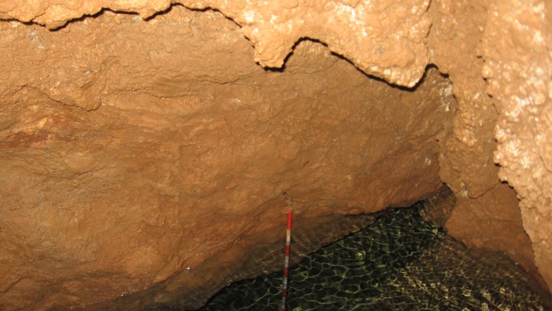 Innenansicht einer Höhle mit Wasser und braunen Felswänden.
