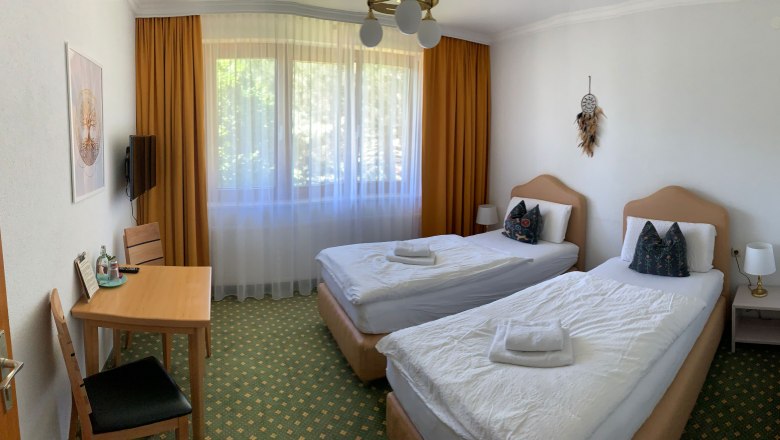 Ein Hotelzimmer mit zwei Einzelbetten, einem Tisch mit Stühlen und einem Fenster mit Vorhängen.