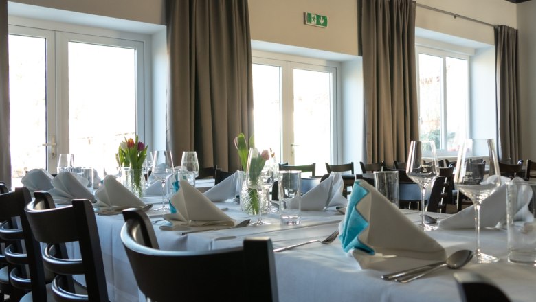 Elegantes Restaurant mit gedeckten Tischen, weißen Tischdecken und gefalteten Servietten.