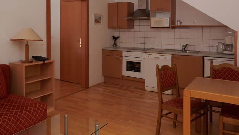 Kompakte Küche mit Holzschränken, Esstisch und Stühlen, Herd, Spüle und Mikrowelle.