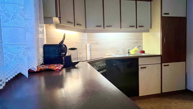 Küche mit dunkler Arbeitsplatte, hellen Schränken und Holzdecke.