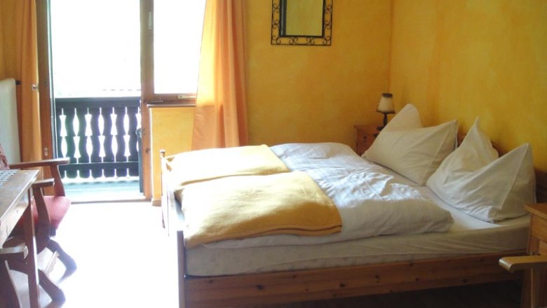 Gemütliches Zimmer mit Holzmöbeln, gelben Wänden und Balkon.