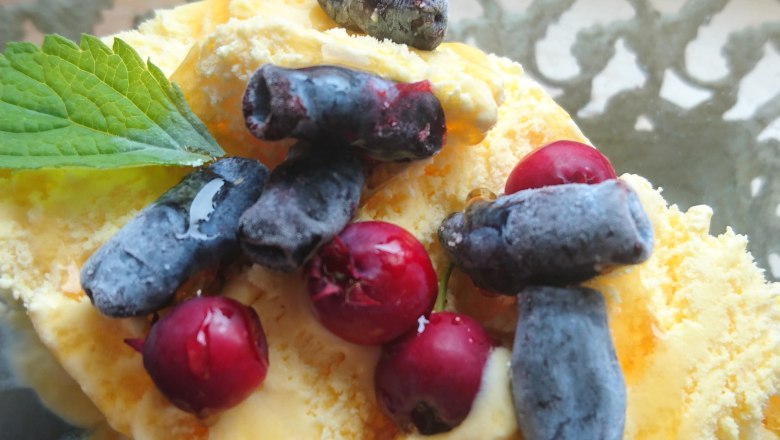 Ein Dessert mit gelbem Eis, roten und blauen Beeren, garniert mit einem gr&uuml;nen Blatt, in einer Glasschale.