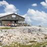 Fischerhütte auf dem Schneeberg mit Wanderern und blauem Himmel.