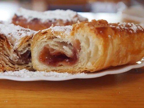 Nahaufnahme von Gebäck mit Fruchtfüllung und Puderzucker auf einem Teller.