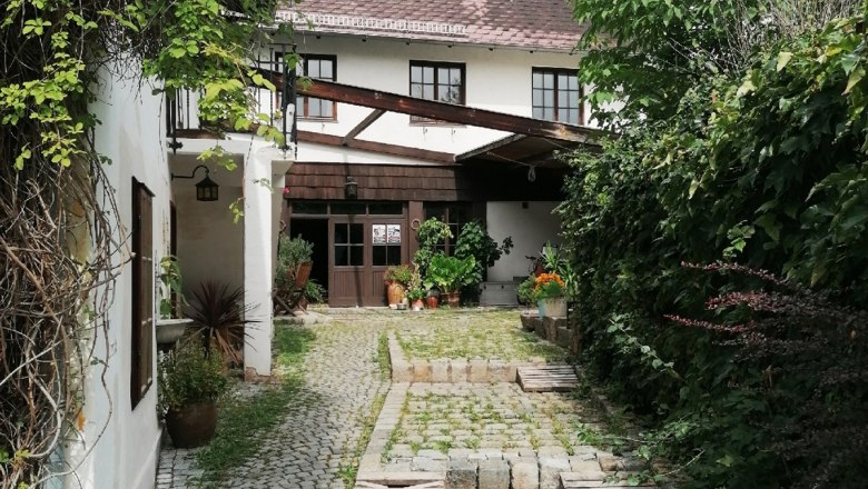 Gepflasterter Hofeingang mit Pflanzen und einem weißen Gebäude im Hintergrund.