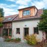 Rustikales Haus mit Ziegeldach und Holzverkleidung, umgeben von Pflanzen und Kopfsteinpflaster.