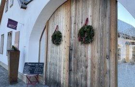 Eingang der Cafe-Bar Mosa mit Holztür und Kränzen.