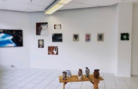 Galerieraum mit Kunstwerken an der Wand und Keramiken auf einem Holztisch.