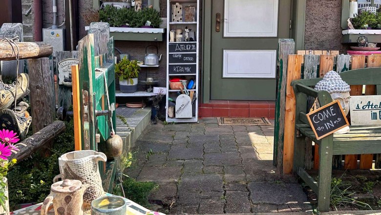 Eingang eines kleinen Ateliers mit dekorativen Elementen und einem Schild mit der Aufschrift 'Come in'.