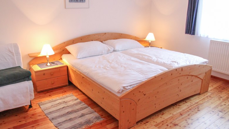 Gem&uuml;tliches Schlafzimmer mit Doppelbett, Holzboden und Nachttischen mit Lampen.