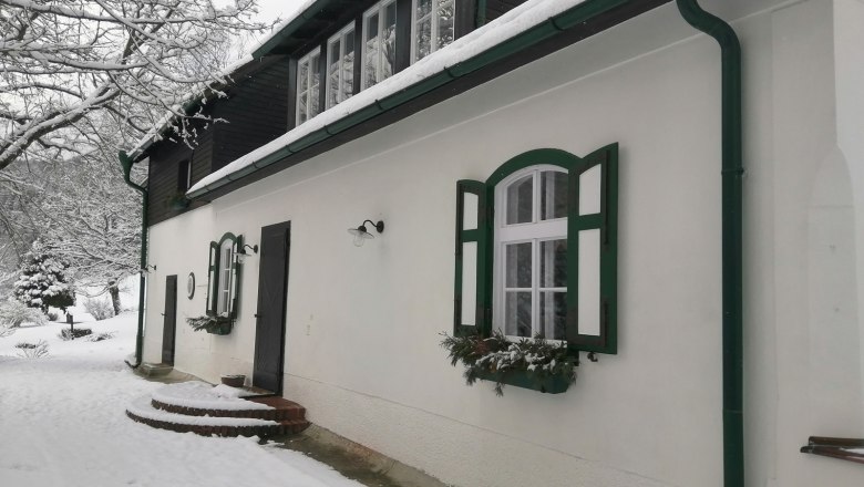 Ein verschneites Haus mit grünen Fensterläden und Dachrinnen.