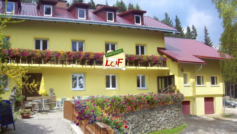 Gelbes Gasthaus mit roten Dächern und blühenden Blumen auf dem Balkon.