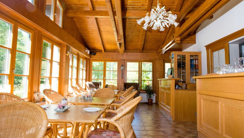 Ein heller Frühstücksraum mit Holzmöbeln, großen Fenstern und einem Kronleuchter.