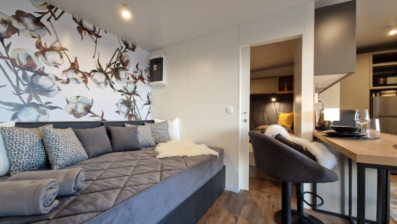 Innenansicht eines modernen Chalets mit grauem Sofa, dekorativer Blumenwand, Barhocker und Esstisch.