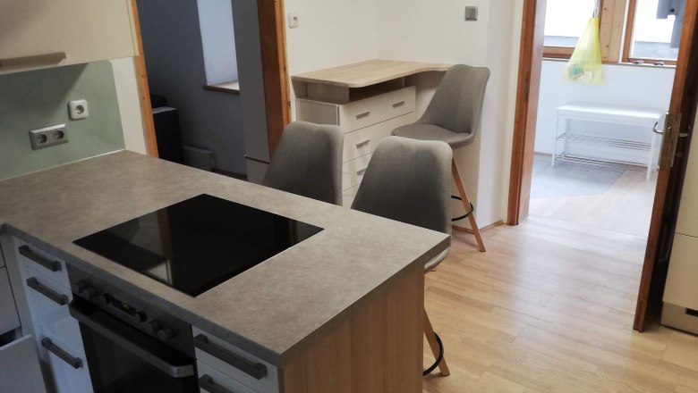 Moderne Küche mit Kochinsel, zwei grauen Stühlen und Holzfußboden.