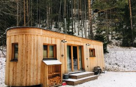Ein Wohnwagon aus Holz steht im verschneiten Wald.
