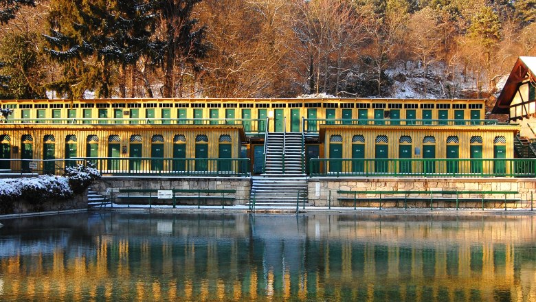 Historisches Thermalbad mit gelben und grünen Kabinen, umgeben von Bäumen im Winter.