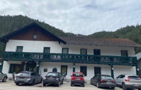 Ein zweist&ouml;ckiges Geb&auml;ude mit gr&uuml;nem Balkon und geparkten Autos davor.