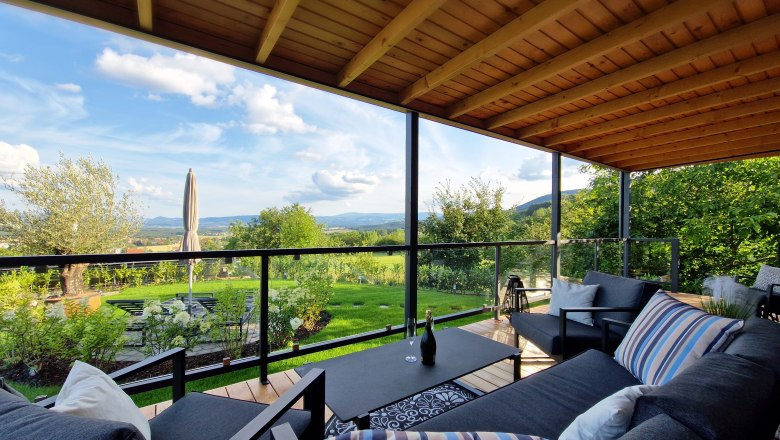 Überdachte Terrasse mit modernen Möbeln und Blick auf grüne Landschaft.