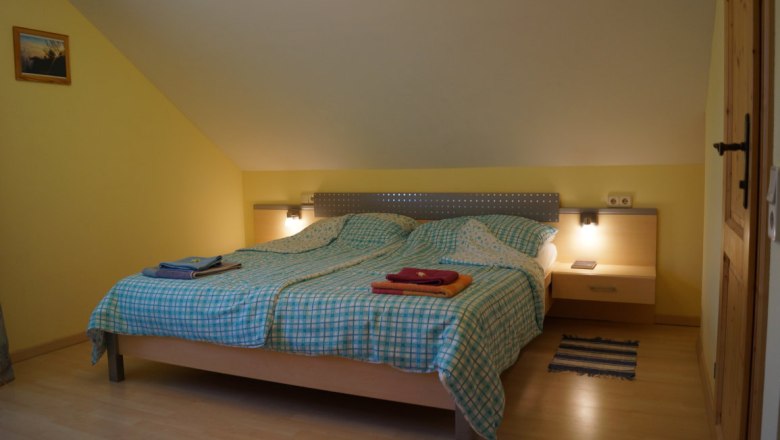 Ein gemütliches Schlafzimmer mit einem Doppelbett, gelben Wänden und einem kleinen Nachttisch mit Lampe.