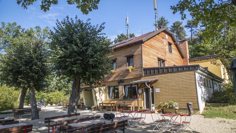 Holzhaus mit Biergarten im Freien, umgeben von B&auml;umen.