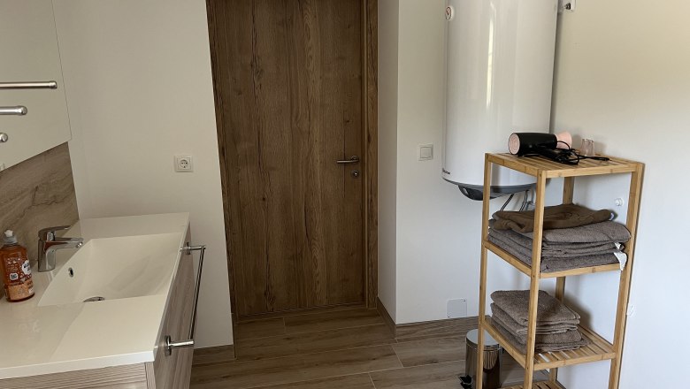 Modernes Badezimmer mit Holzregal, Handtüchern, Waschbecken und Warmwasserboiler.