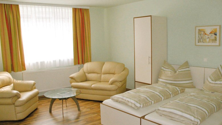 Helles Zimmer mit zwei Betten, Sofas, einem Tisch und einem Schrank.