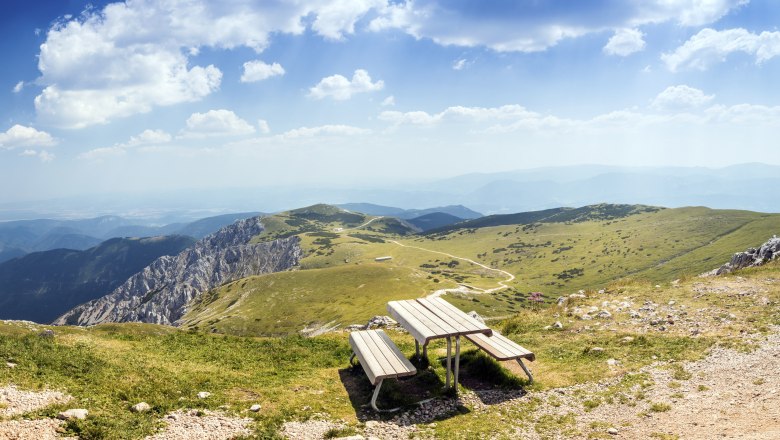 Panoramablick von einem Berg mit einer Bank im Vordergrund und grünen Hügeln im Hintergrund.
