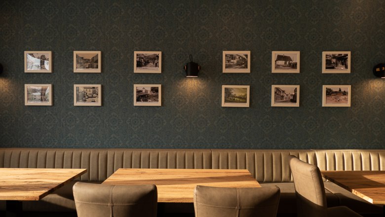 Innenansicht eines Restaurants mit gepolsterten Bänken und Holztischen, dekoriert mit gerahmten Fotos an der Wand.