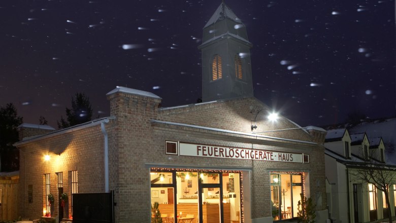 Altes Feuerwehrhaus bei Nacht mit Lichtern und Schneefall.