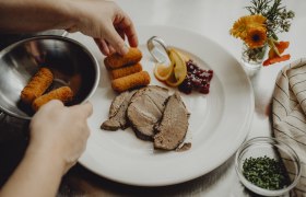 Ein Teller mit Fleisch, Kroketten, Preiselbeeren und Zitronenscheiben wird angerichtet.